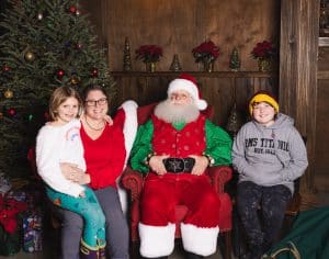 Mom and two daughters sit next to Santa and smile
