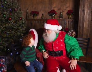 Curly red-haired young boy smiles up at Santa