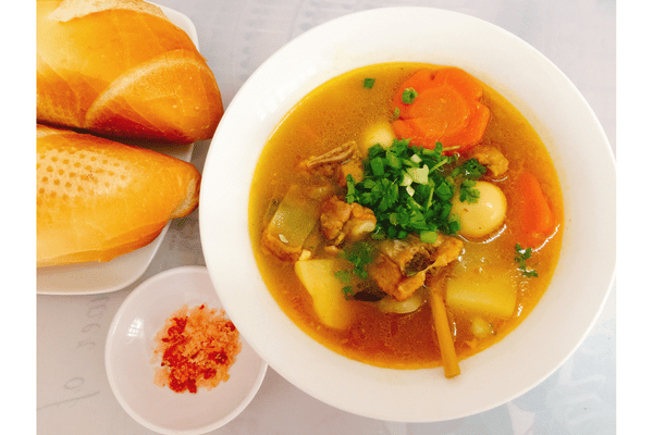 a bowl of soup with a side of rolls