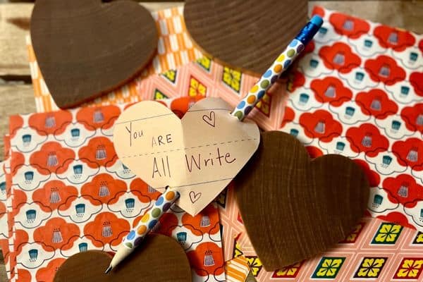 Colorful paper with wooden hearts on top. In the middle is an easy valentine's heat that says you are all write with a pencil through it.