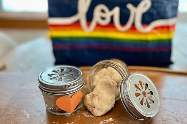 Two small jars of play dough on a table with a background that says love for an easy preschool valentine
