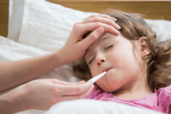 mother's hand on feverish child's forehead while taking her temperature