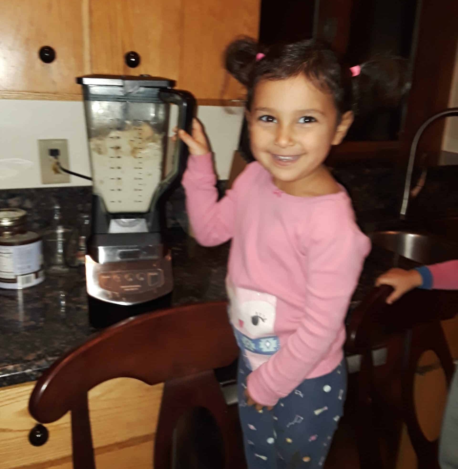 young girl on a chair mixing ingredients for a healthy chocolate dessert in the blender