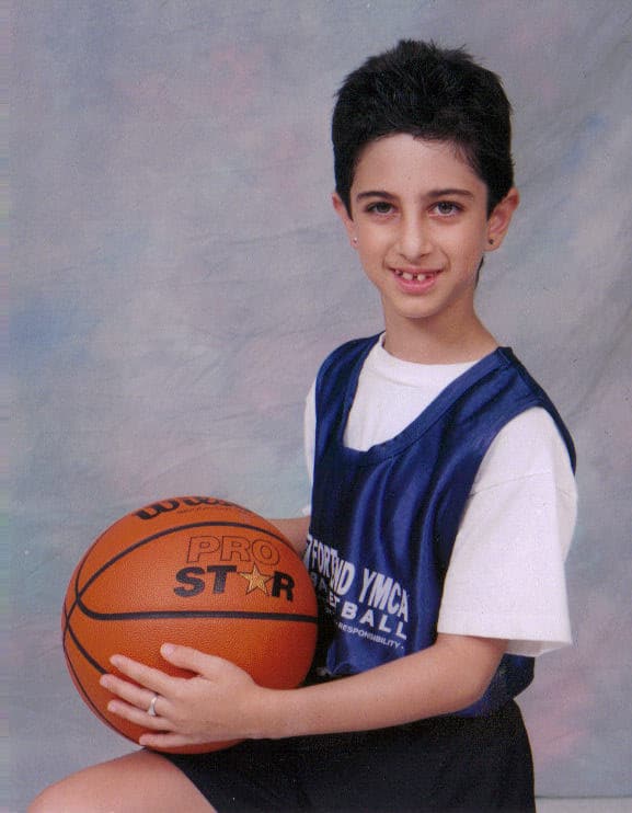 7 year old girl with short hair wearing basketball uniform and holding a basketball kneels for a photo. She began to bullied a lot around this time.