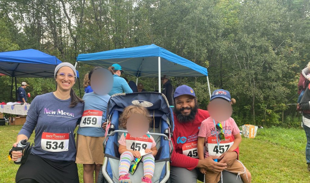 Davida posing with her husband and three young kids, including one in a stroller, outside in a field all wearing race bibs before a running race.