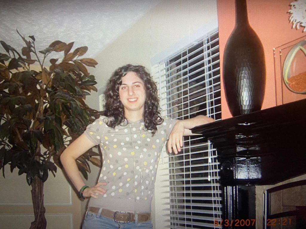 17 year old Davida, now with long hair, poses next to a fire place