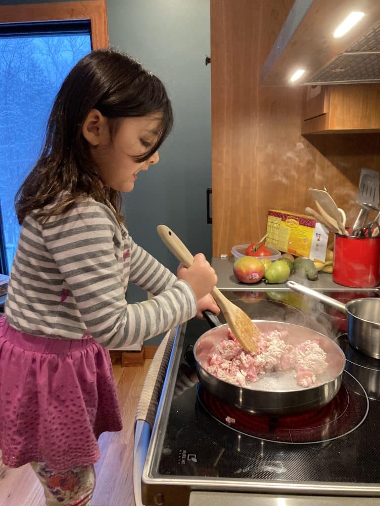 child stands on a chair to cook at a stove