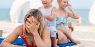 The Excruciating Pressure of Modern Motherhood mom holding her head while two children sit on her pressure of modern motherhood
