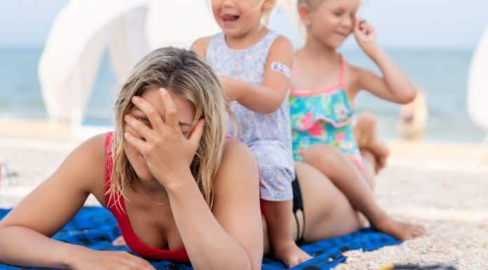 The Excruciating Pressure of Modern Motherhood mom holding her head while two children sit on her pressure of modern motherhood
