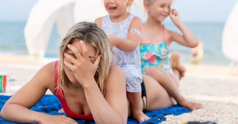 mom holding her head while two children sit on her pressure of modern motherhood