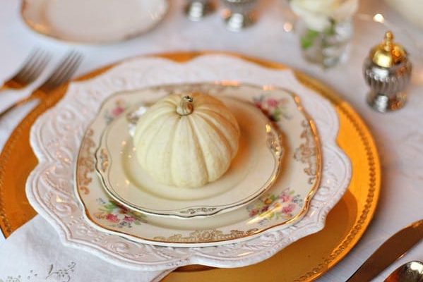 small white gourd on a stack of fancy plates showing a silly example of a manageable Thanksgiving meal for small families.