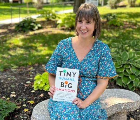 Alyssa Blask Campbell sits outside holding her book, Tiny Kids, Big Emotions