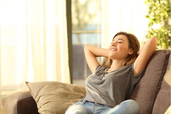 A woman relaxing on the couch with her arms behind her head. What questions to ask before a drop off playdate?