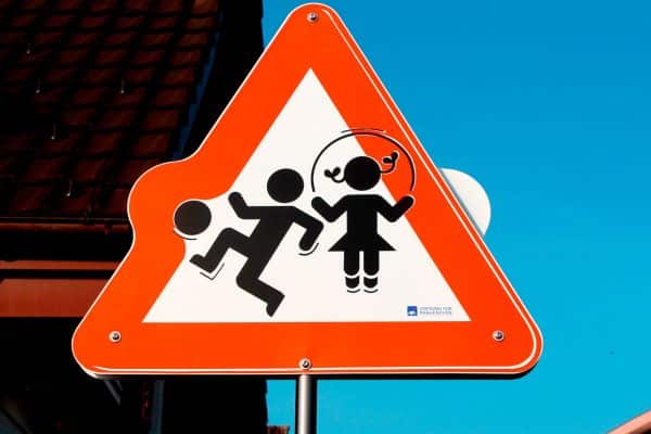 A triangular safety sign with a white background and red border. Inside it has a drawing of a child kicking a ball and a child jumping rope. What are the questions to ask before a drop off playdate?