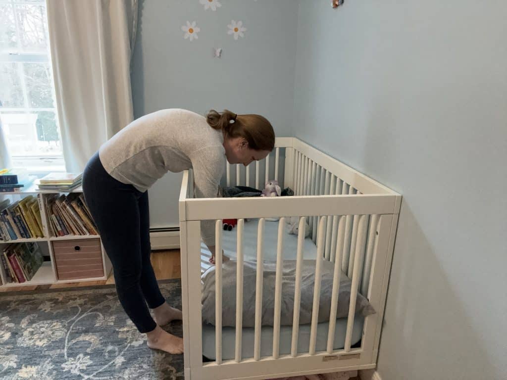 mother bends over a baby's crib in a posture that is likely to injure her back