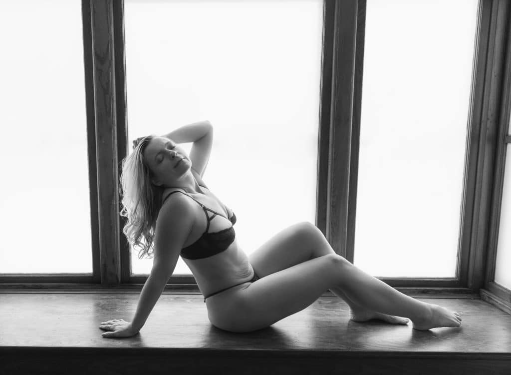 Woman in front of a frosted, back-lit window while doing boudoir photography with Hillary Dubie