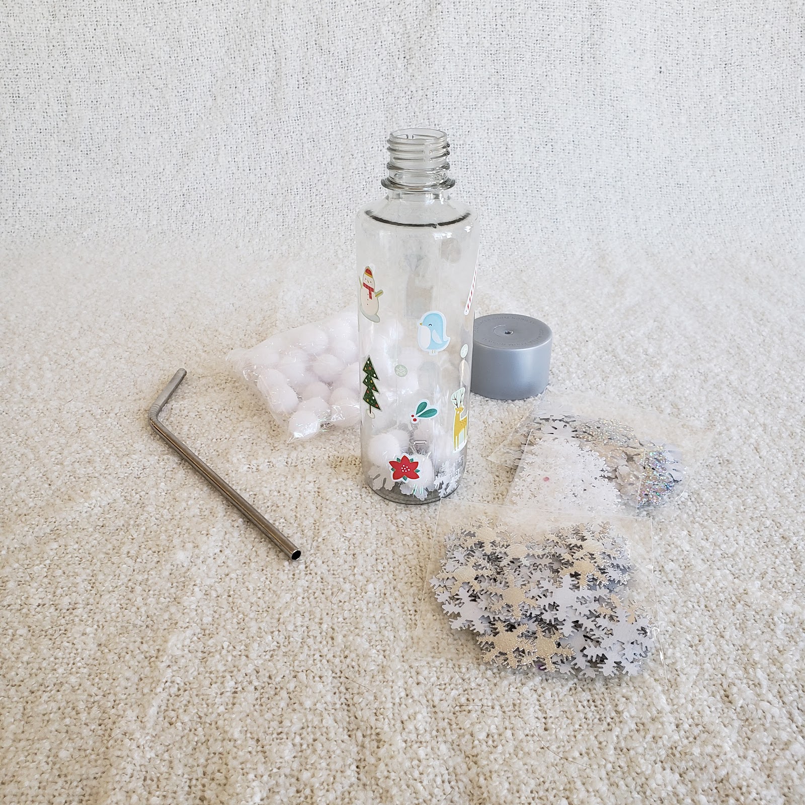 empty clear water bottle, craft poms, confetti, and a straw- ready to be assembled into a no mess snow globe