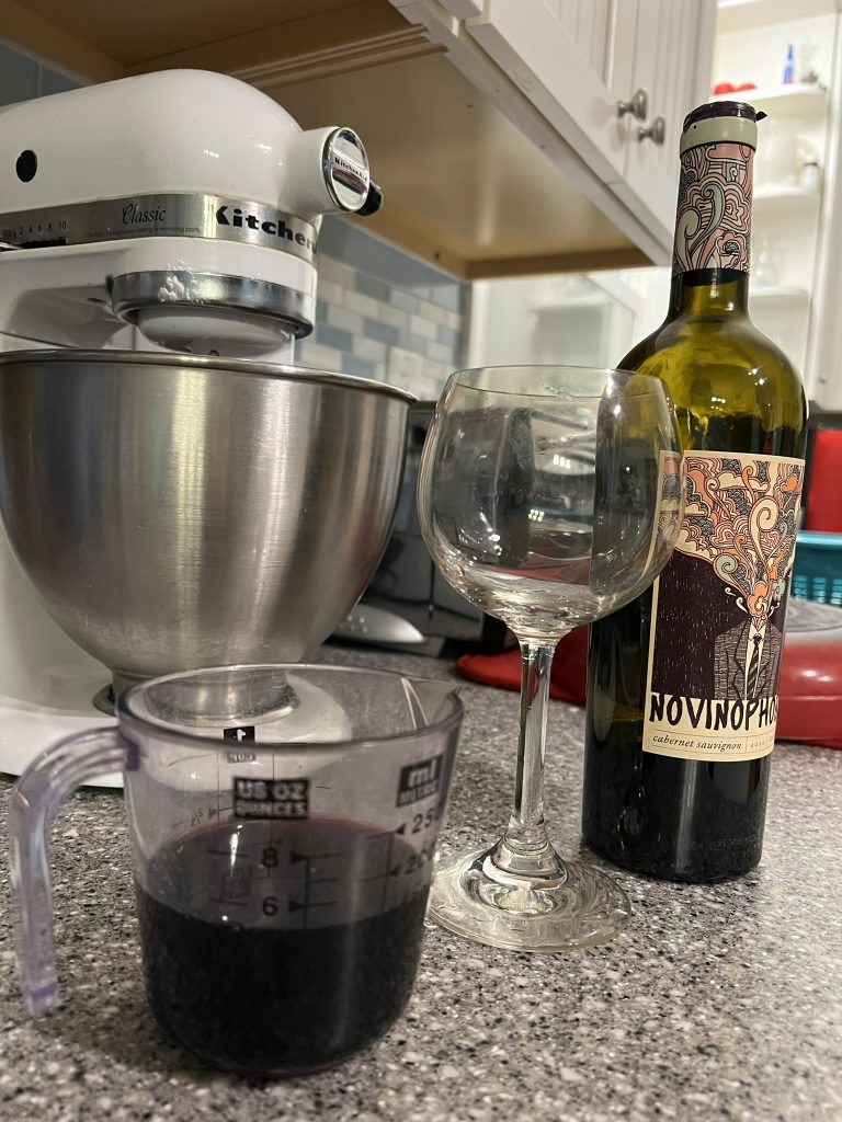 Glass of wine next to a measuring cup with wine in it