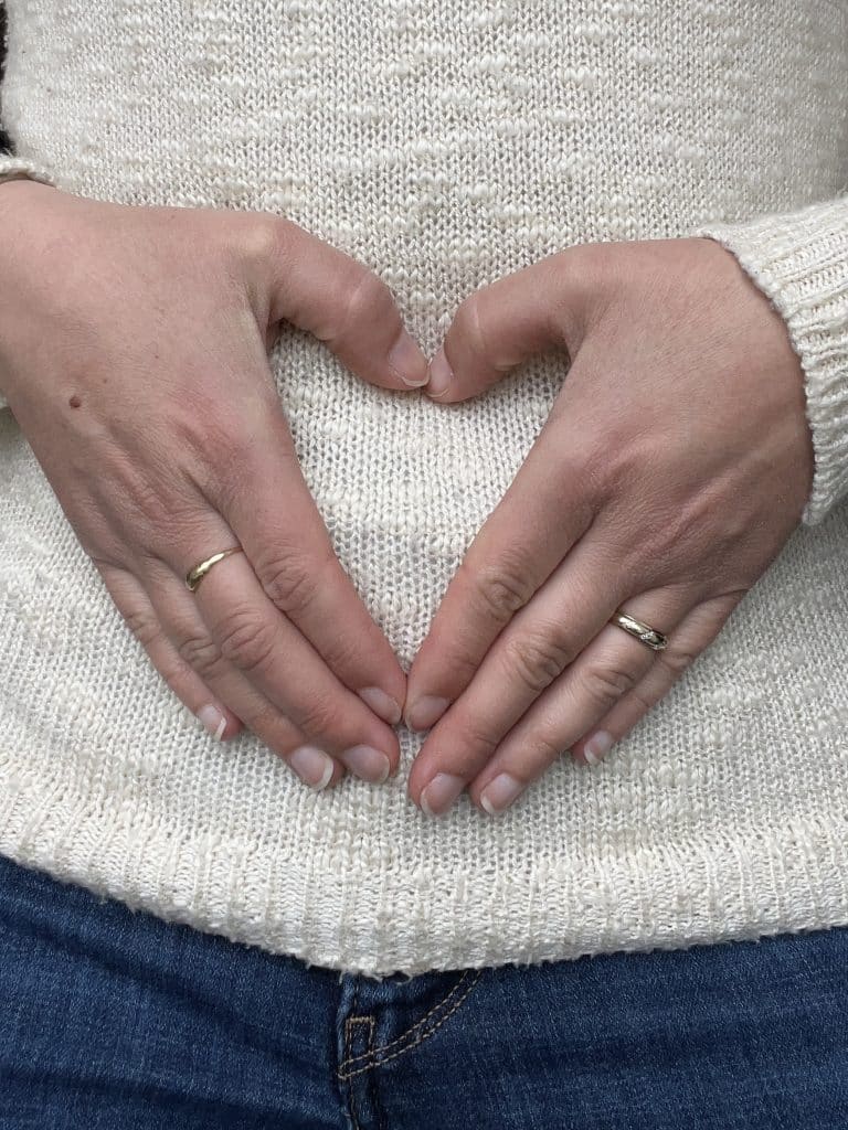 woman's hands in a hart shape over her belly