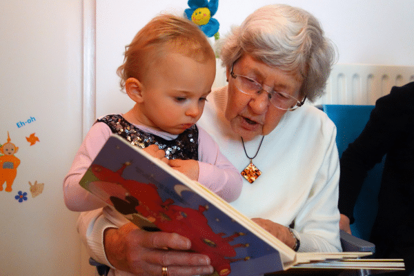 Old woman reading a cardboard picture book to a very young child.