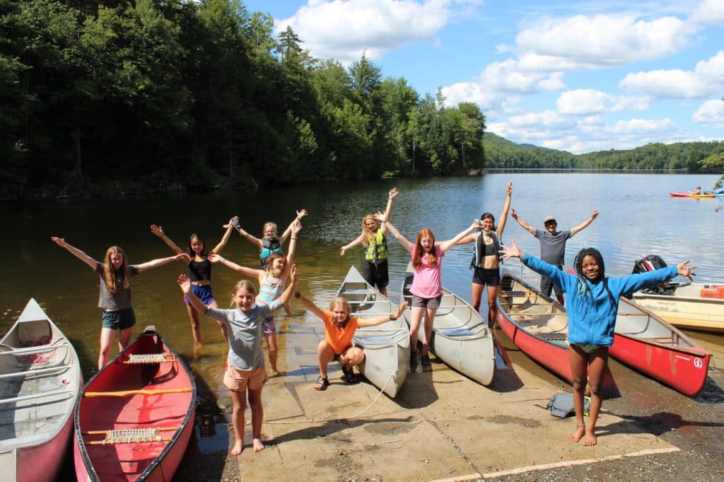 Joyous Water Wanderings campers with arms spread wide, in front of the Green River Reservoir in Vermont.