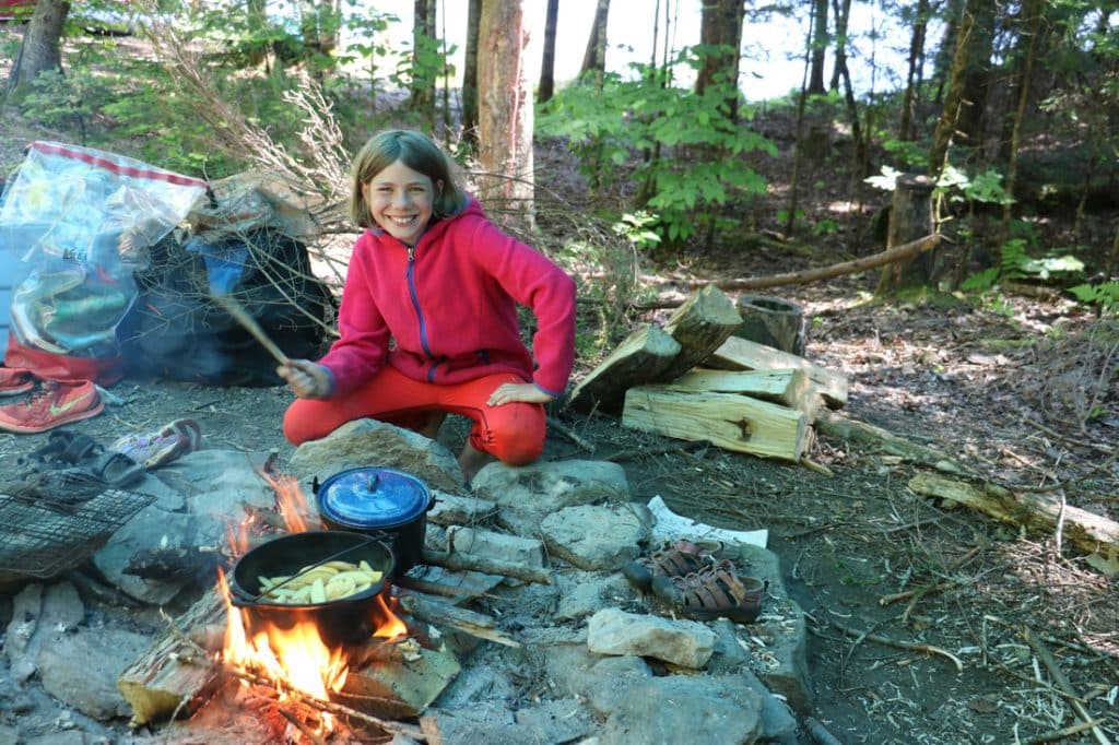 Camper with a giant grin cooks over an open fire.