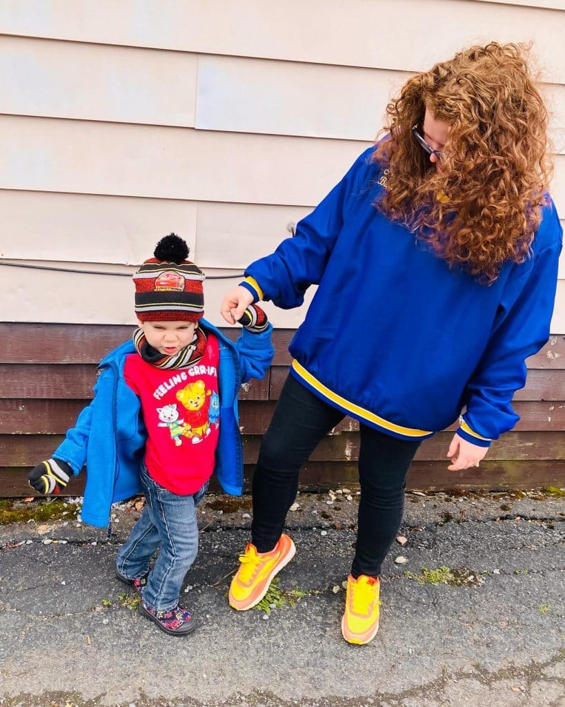Mom with red, curly hair holding her 4 year old son's hand. They are outside.