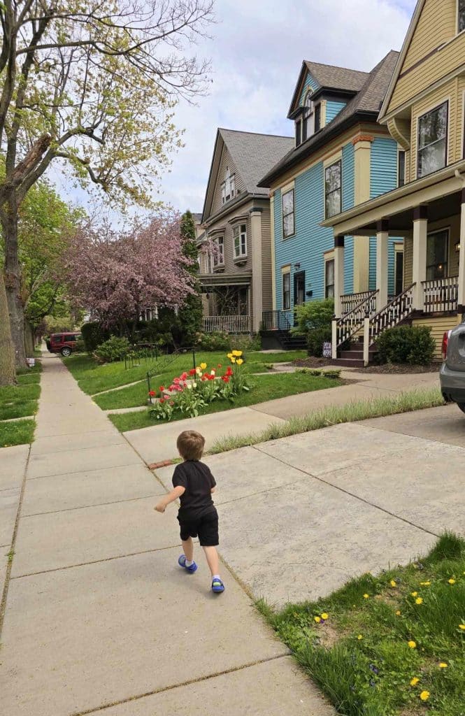 4 year old boy runs down a suburban sidewalk in the spring