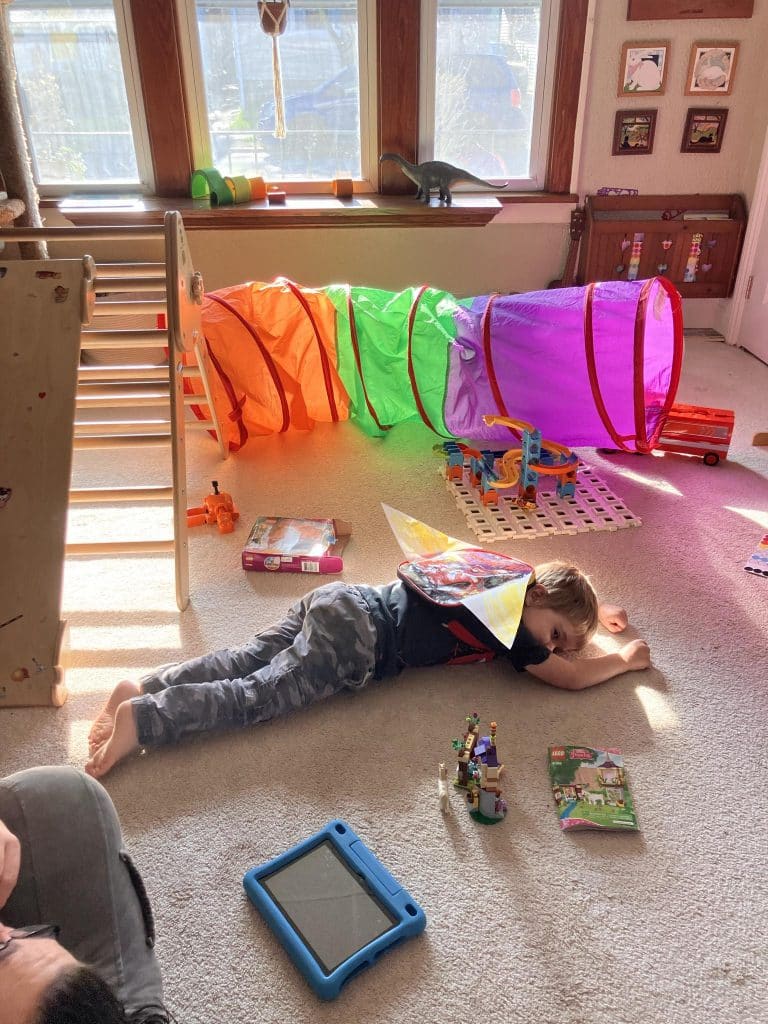 4 year old asleep on the playroom floor, wearing a homemade jetpack.