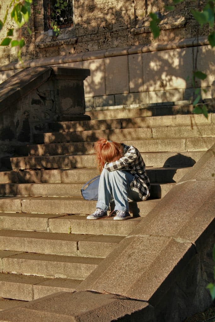 Teen girl sitting on concrete steps in the sun with her head in her hands.