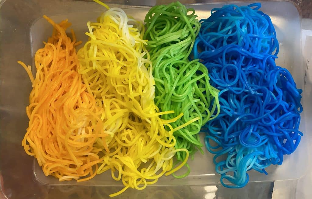 Celebrating pride as a queer mom of a baby with rice noodles dyed orange, yellow, green, and blue.