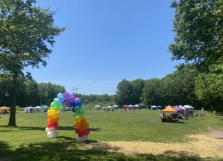 Celebrating Pride as a Queer Mom Rainbow balloon arch leads to a field with vendor tents around the edge.
