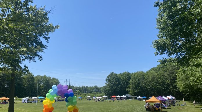 Celebrating Pride as a Queer Mom Rainbow balloon arch leads to a field with vendor tents around the edge.