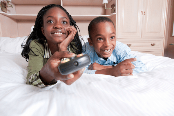 Two kids watching tv in bed.