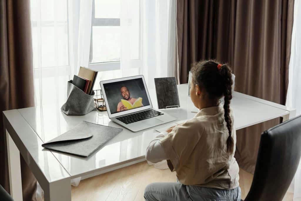 Child sitting in front of a computer. There is an image of someone reading on the computer screen.