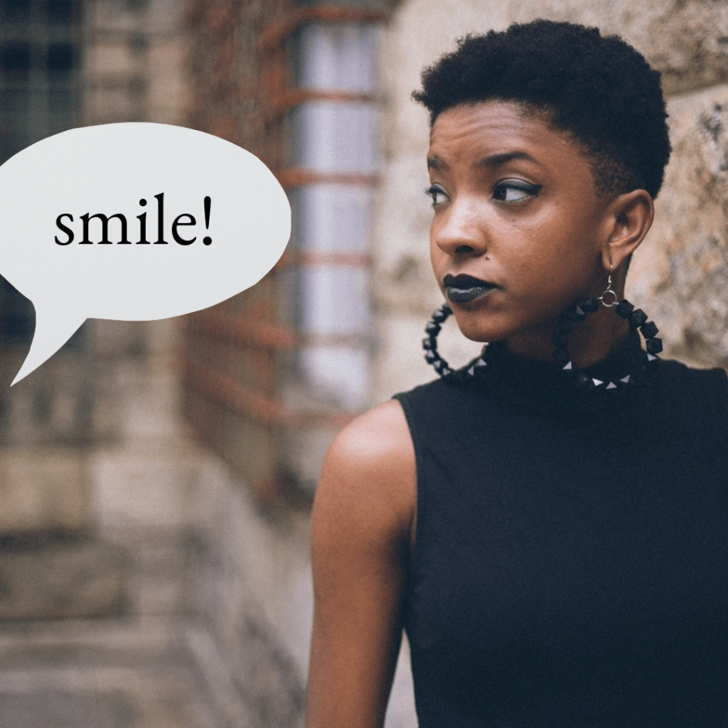Female presenting person staring to their right toward a speech bubble, which comes from someone out of the frame. Speech bubble caption reads: "Smile!"
