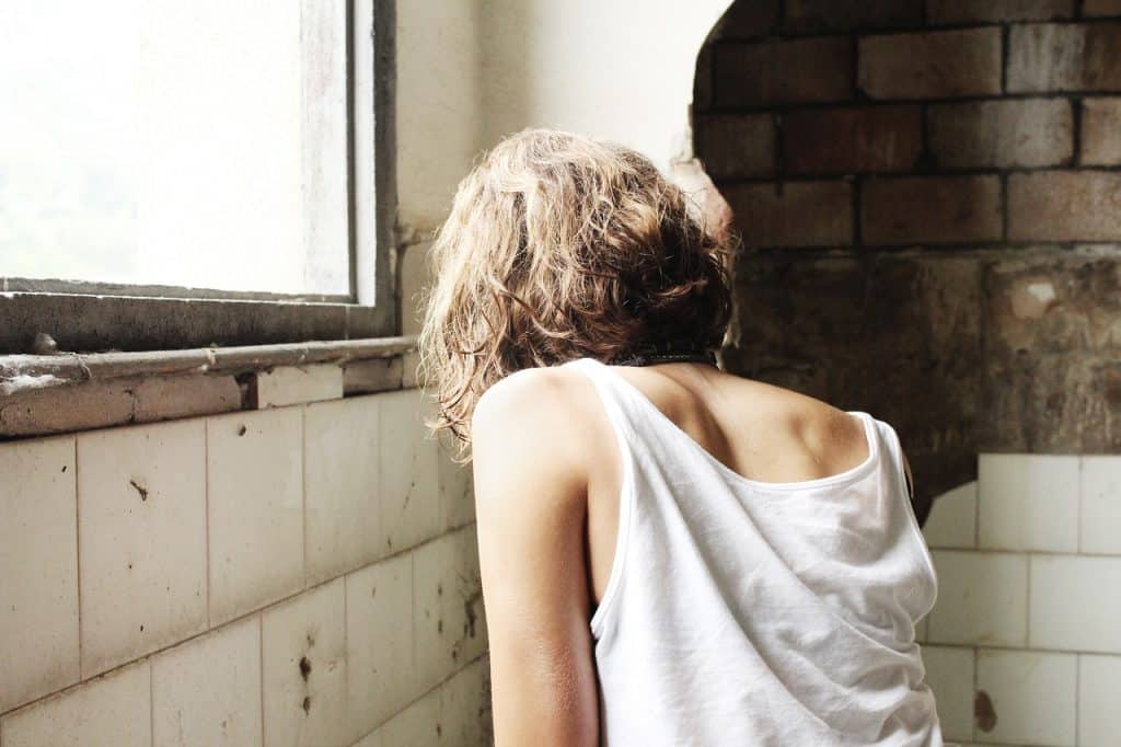 Person with back to camera, head bent down against a decrepit wall, adjacent to a window.