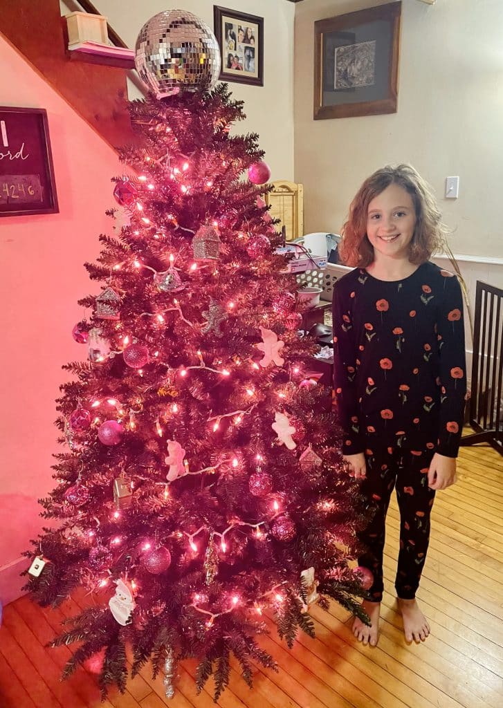 happy pre-teen in front of a pink Christmas tree