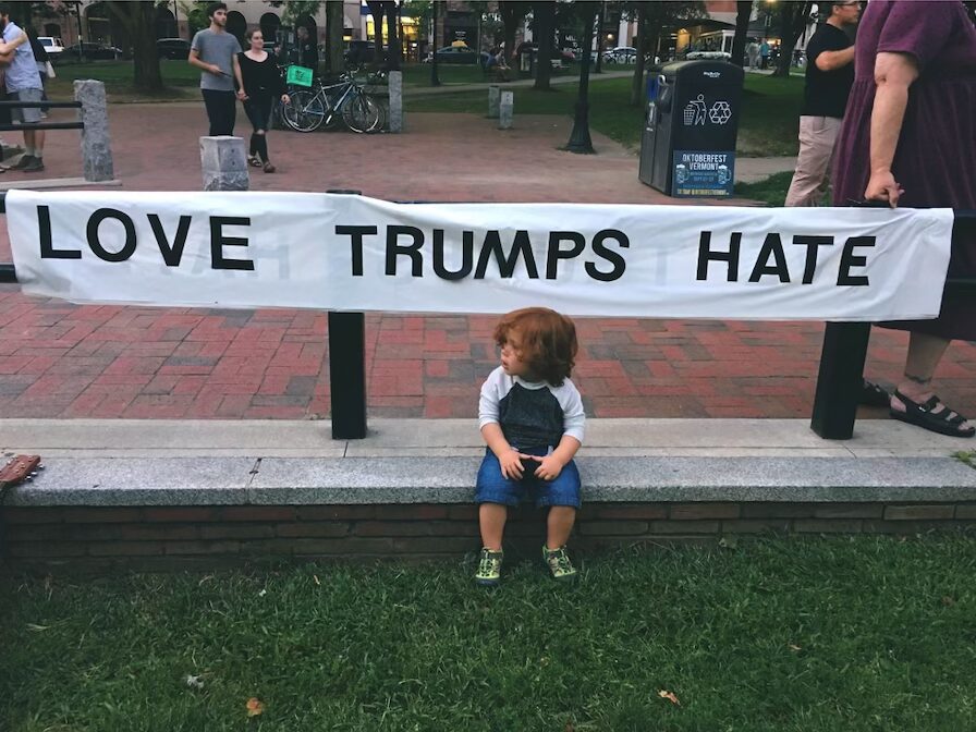 child sits under a sign that says "Love Trumps Hate"