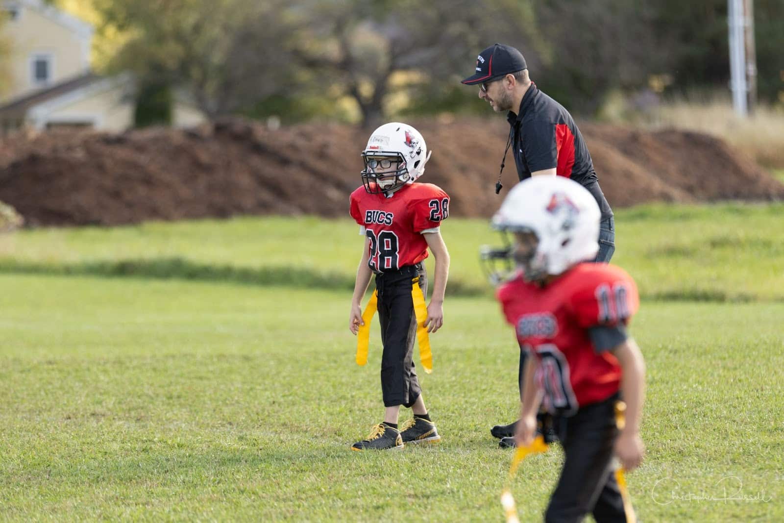 Youth football coach speaking with a young flag football player with glasses