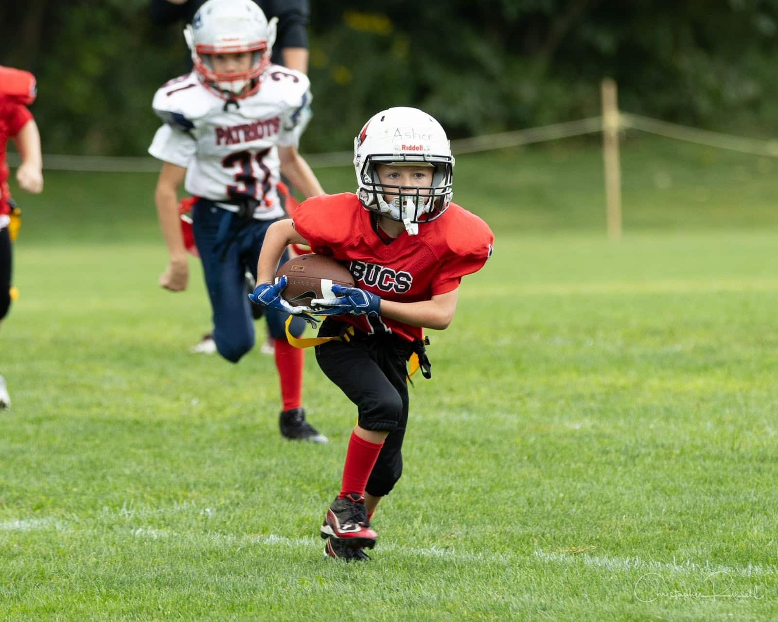 Young football player runs with the ball. He is pursued by an opposing team's player.