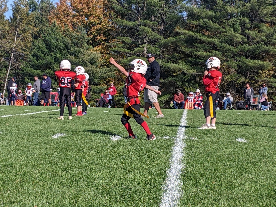 Flag football players on the field, one is stretching his arms out to either side.