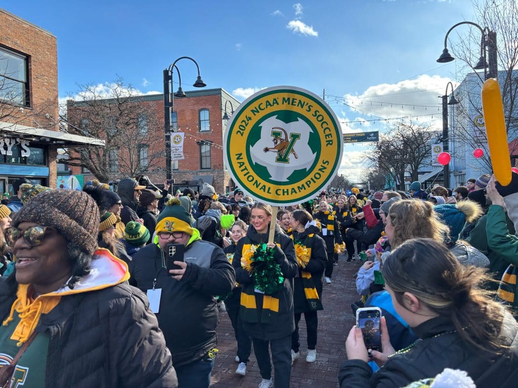 University of Vermont students walking down the street during a celebatory parade surrounded by a large crowd
