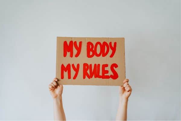 two hands holding up a sign saying my body my rules.