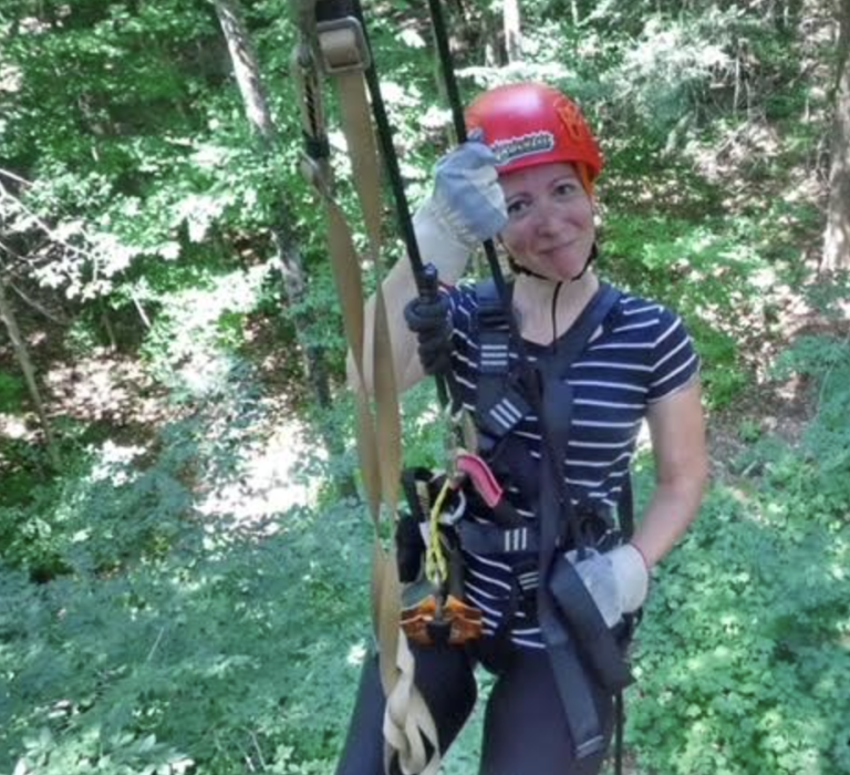 woman on a zipline, smiling and wearing a red helmet